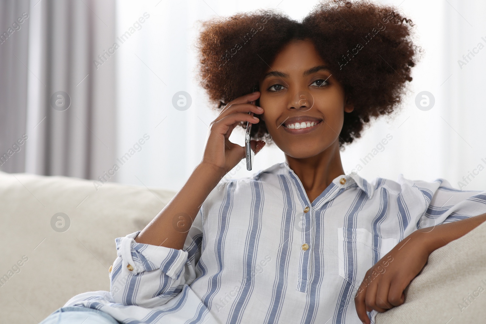 Photo of Smiling African American woman talking on smartphone at home. Space for text