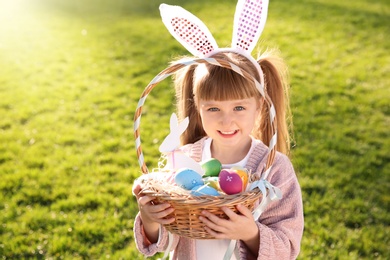 Cute little girl with bunny ears and basket of Easter eggs in park