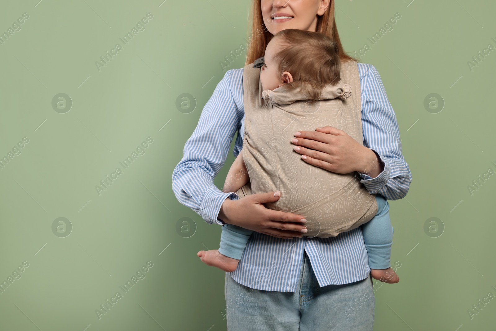 Photo of Mother holding her child in sling (baby carrier) on olive background, closeup