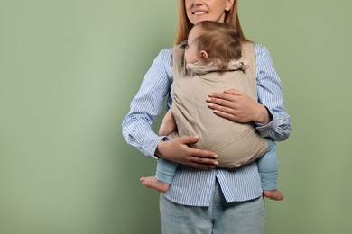 Photo of Mother holding her child in sling (baby carrier) on olive background, closeup