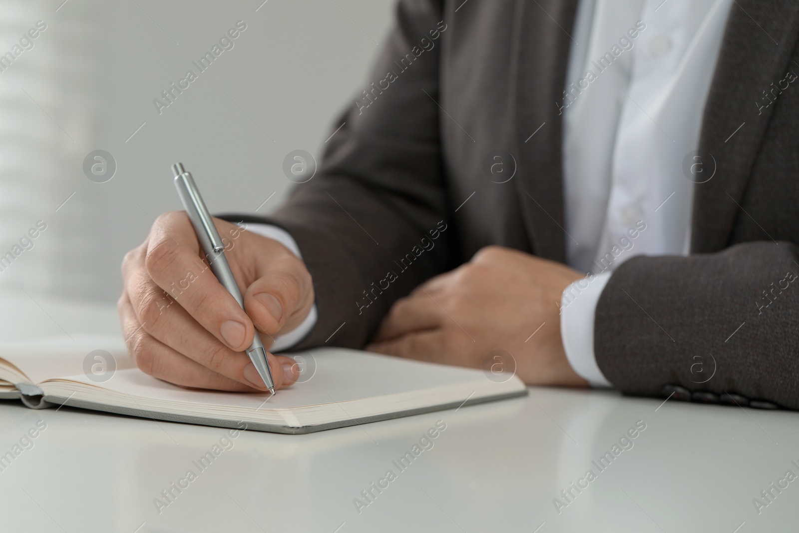 Photo of Man writing in notebook at white table, closeup