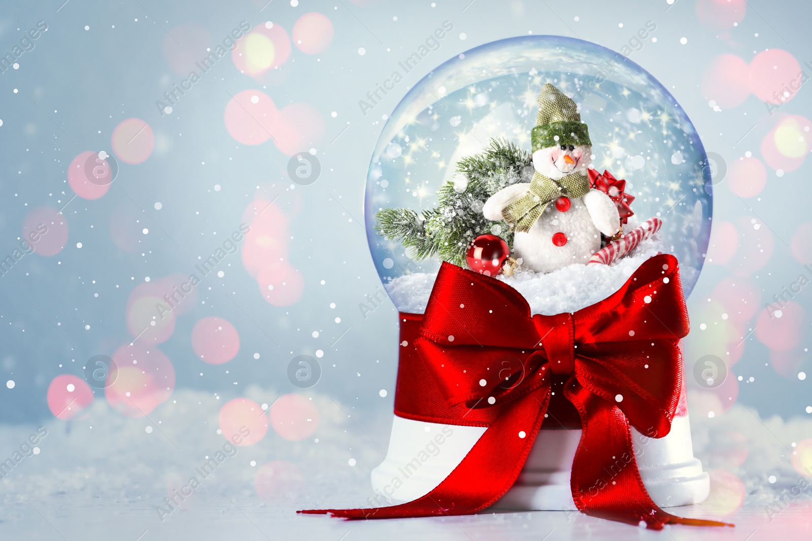 Image of Beautiful snow globe with snowman on table against light background, space for text. Bokeh effect