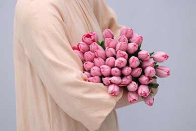 Photo of Woman holding bouquet of pink tulips on light grey background, closeup