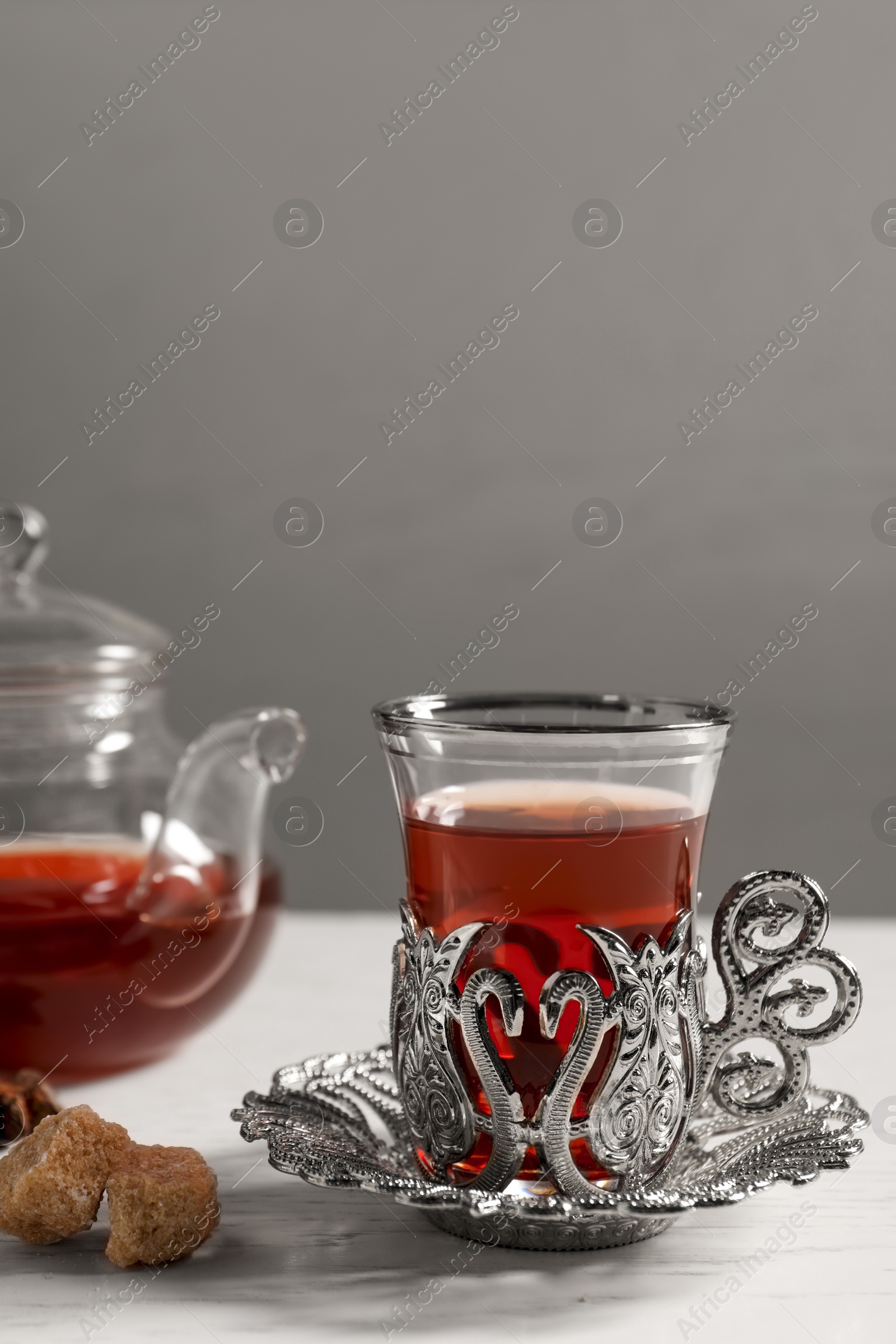 Photo of Glass of traditional Turkish tea in vintage holder with sugar on white table