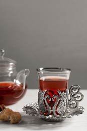 Photo of Glass of traditional Turkish tea in vintage holder with sugar on white table