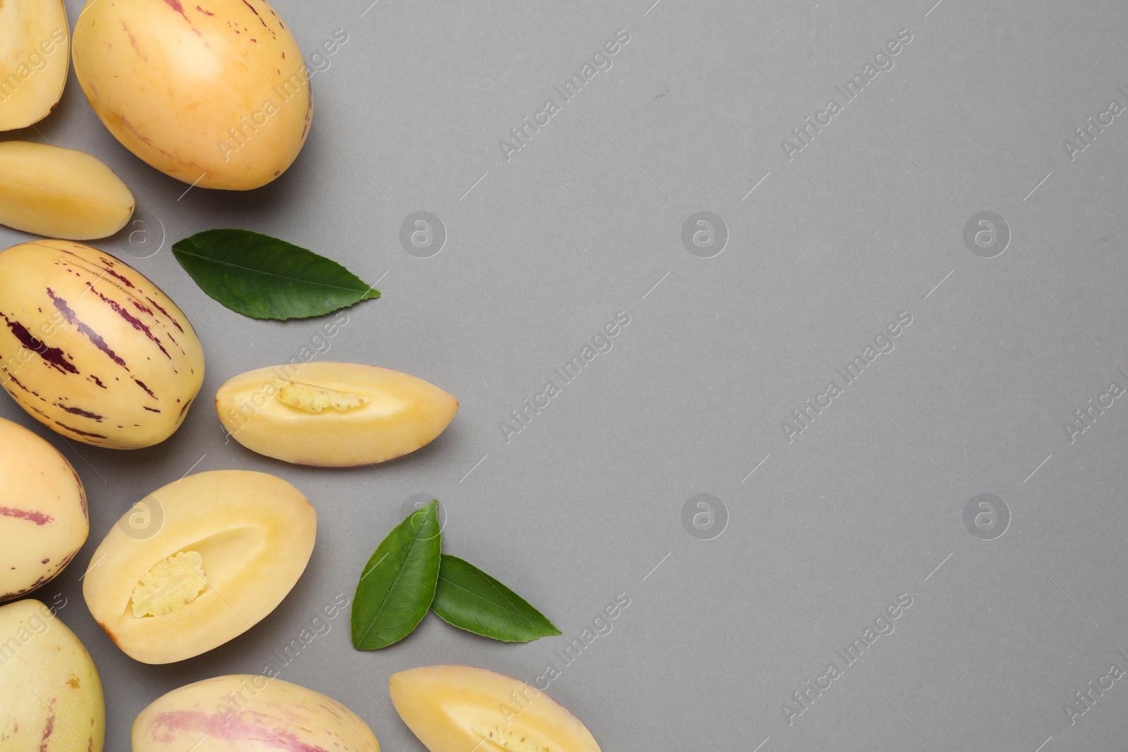 Photo of Whole and cut pepino melons on grey background, flat lay. Space for text