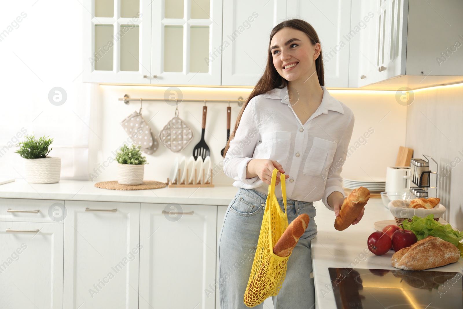 Photo of Woman holding string bag with baguettes in kitchen