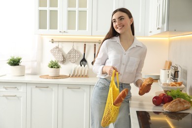 Woman holding string bag with baguettes in kitchen