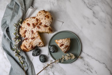 Photo of Delicious Italian Easter dove cake (traditional Colomba di Pasqua), painted eggs and branches with beautiful flowers on white marble table, flat lay