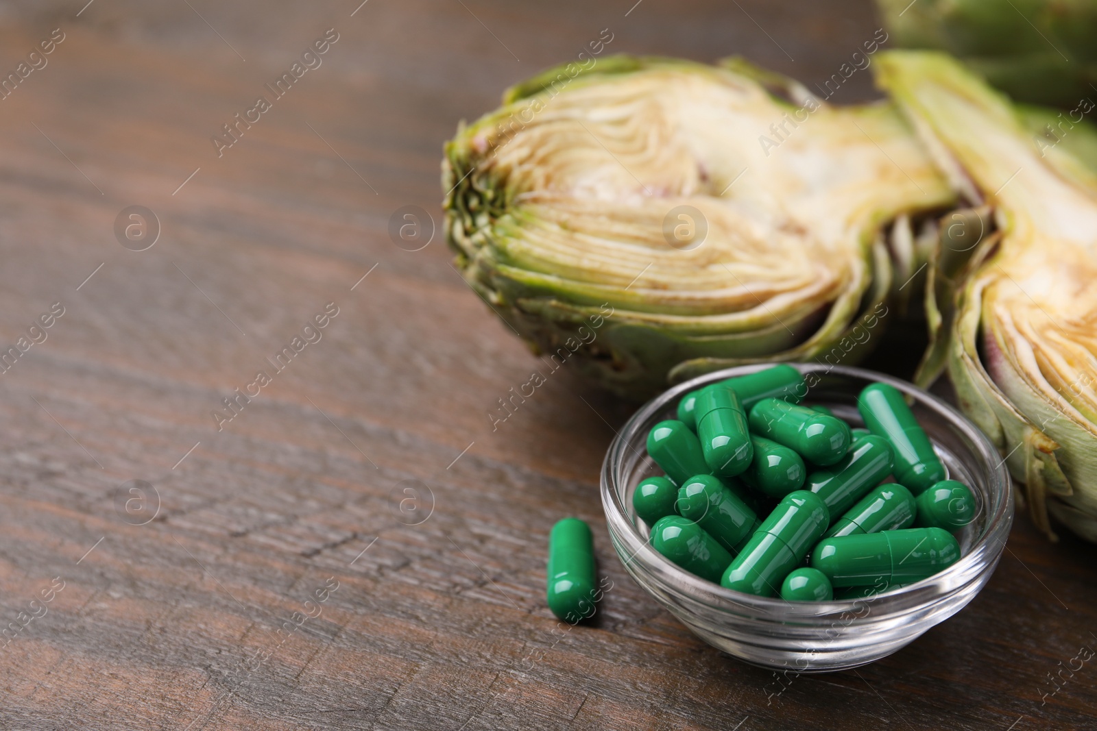 Photo of Bowl with pills and fresh artichokes on wooden table, closeup. Space for text