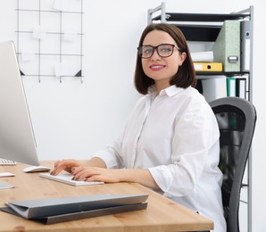 Happy young intern working with computer at table in modern office