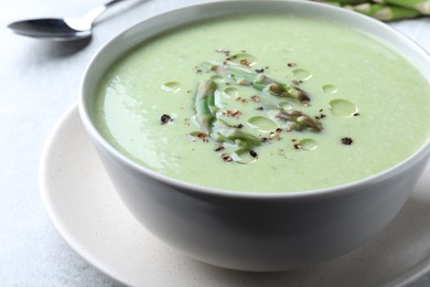 Photo of Delicious asparagus soup served on light grey table, closeup