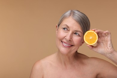 Photo of Beautiful woman with half of orange rich in vitamin C on beige background, space for text
