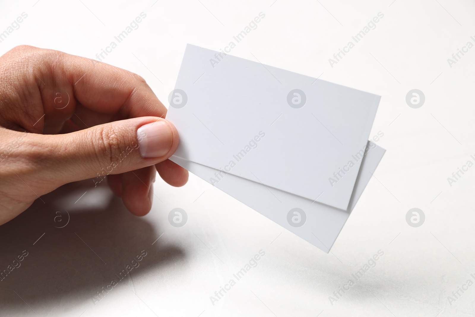 Photo of Man holding blank cards at white table, closeup. Mockup for design