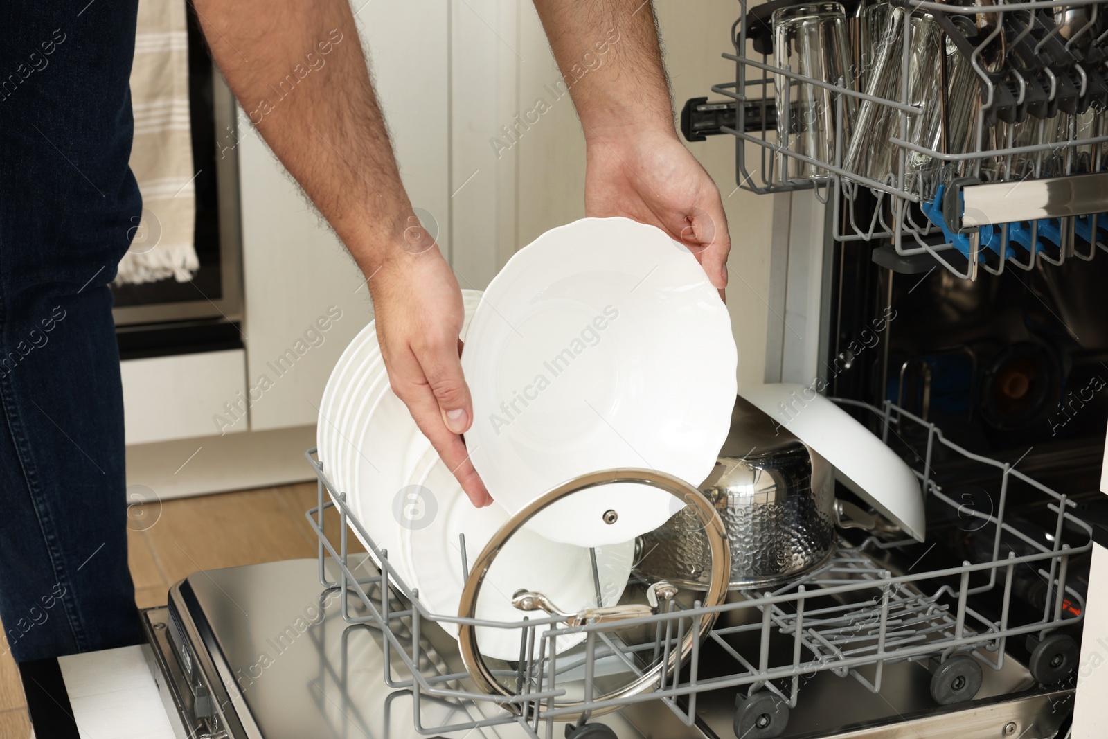 Photo of Man loading dishwasher with plates indoors, closeup