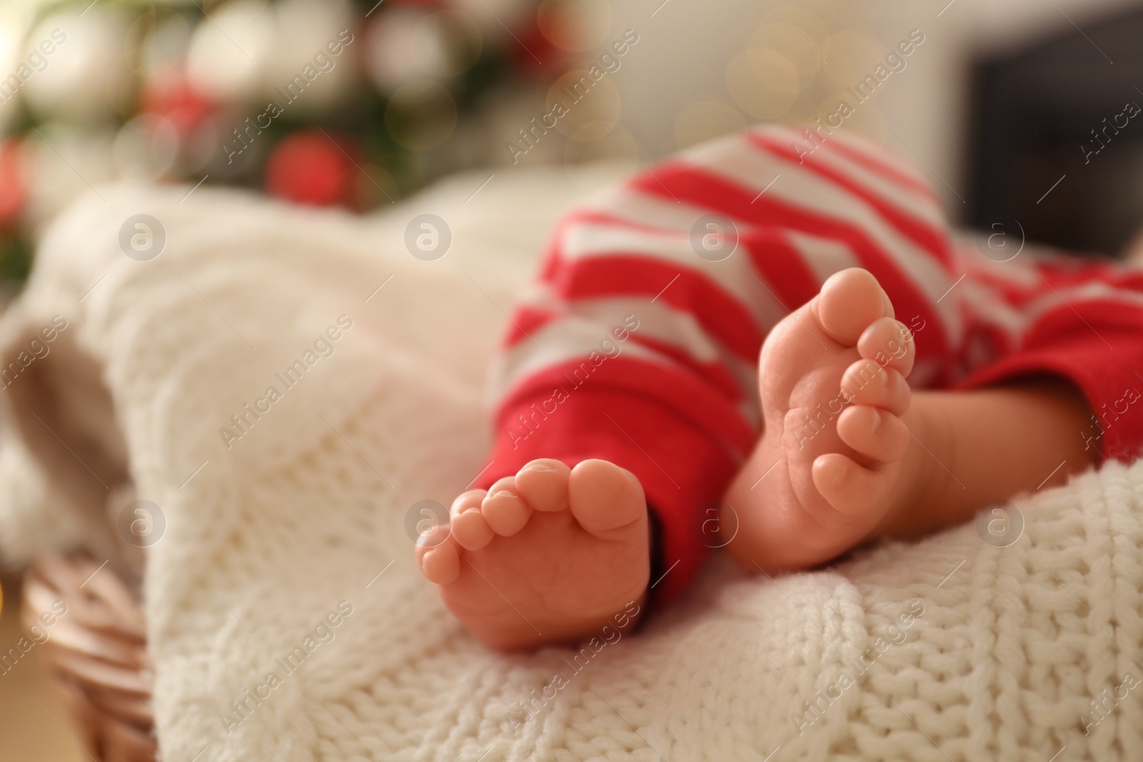 Photo of Cute little baby on knitted blanket in room with Christmas tree, closeup