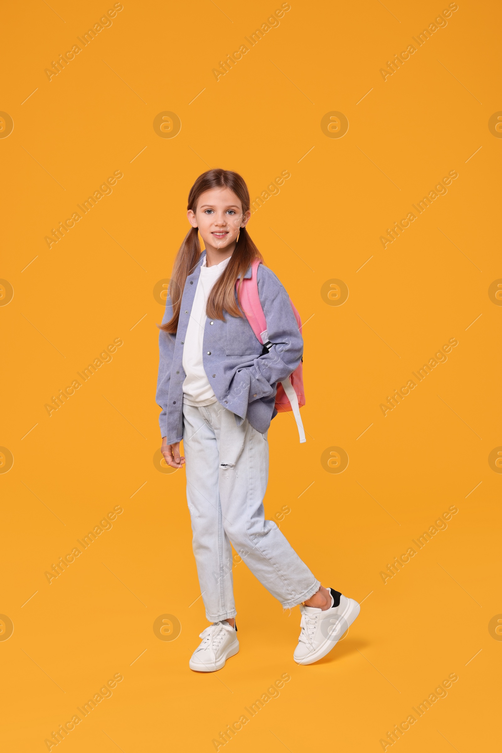 Photo of Happy schoolgirl with backpack on orange background