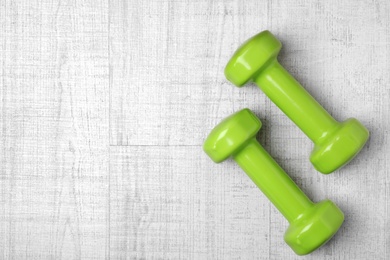 Bright dumbbells and space for text on wooden background, flat lay. Home fitness