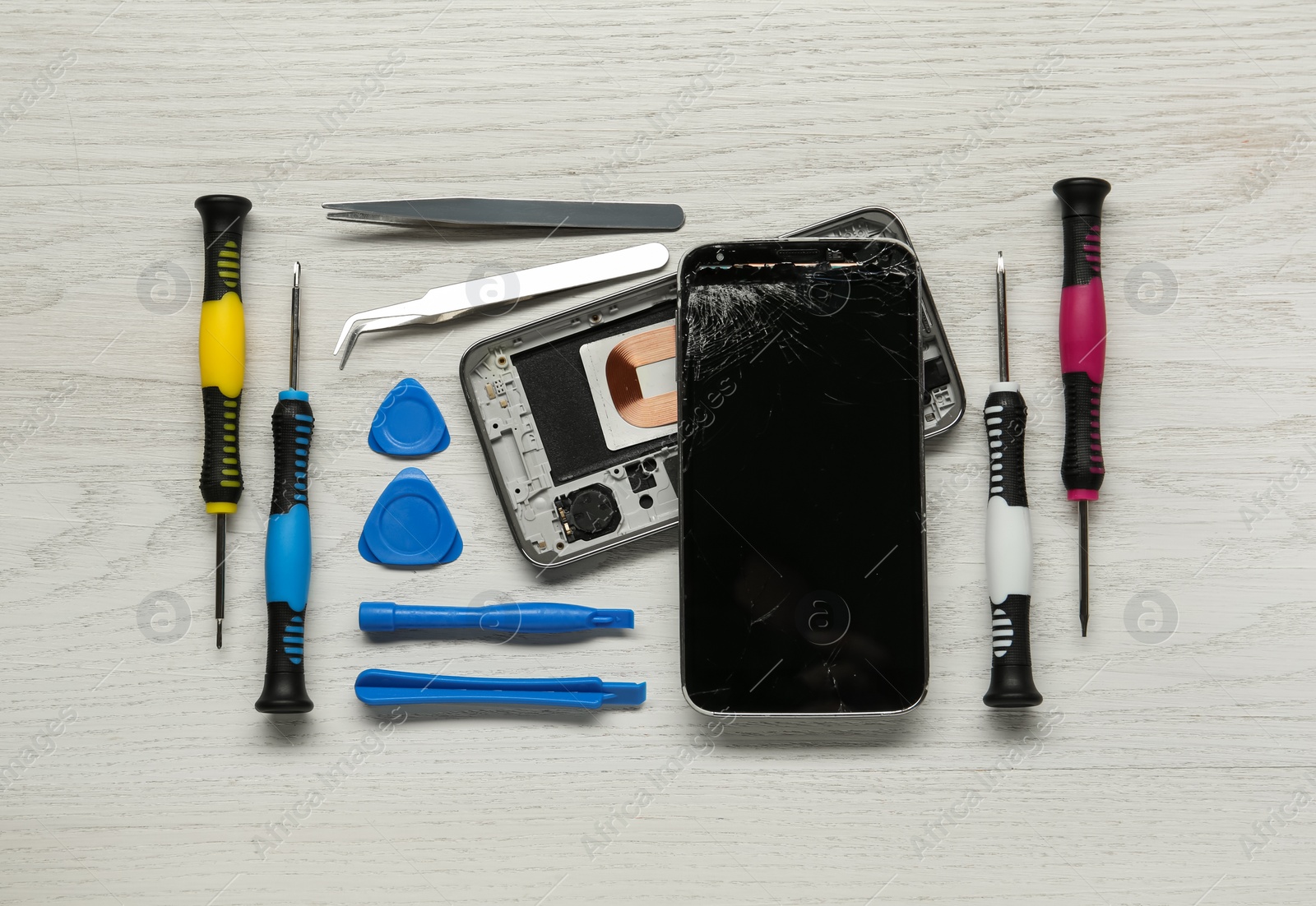 Photo of Damaged smartphone and repair tools on wooden background, flat lay