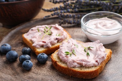 Photo of Tasty sandwiches with cream cheese, thyme and blueberries on wooden tray, closeup