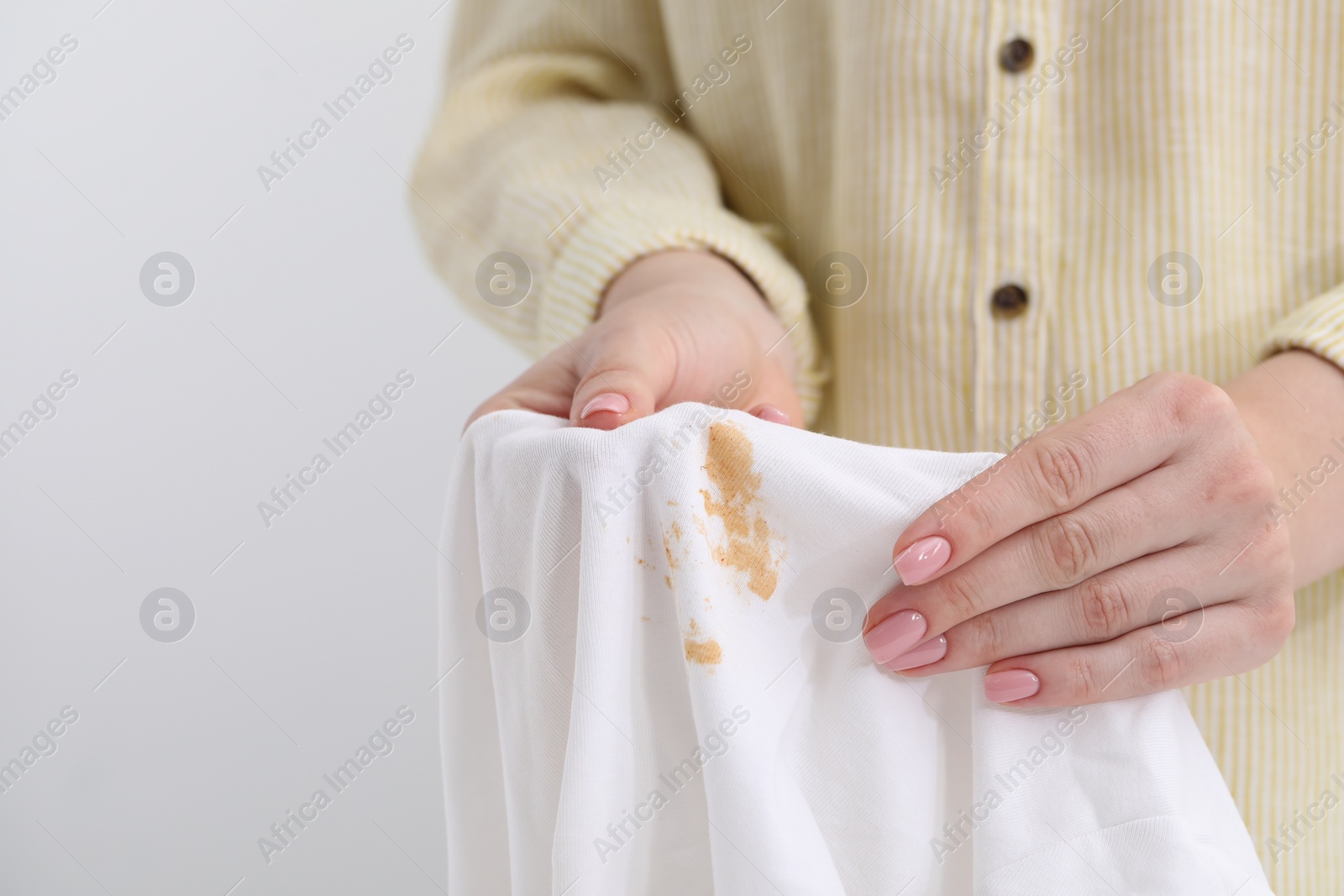 Photo of Woman holding shirt with stain against light background, closeup