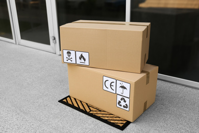 Photo of Cardboard boxes with different packaging symbols on door mat near entrance. Parcel delivery