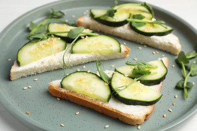 Tasty cucumber sandwiches with sesame seeds and pea microgreens on colorful plate, closeup