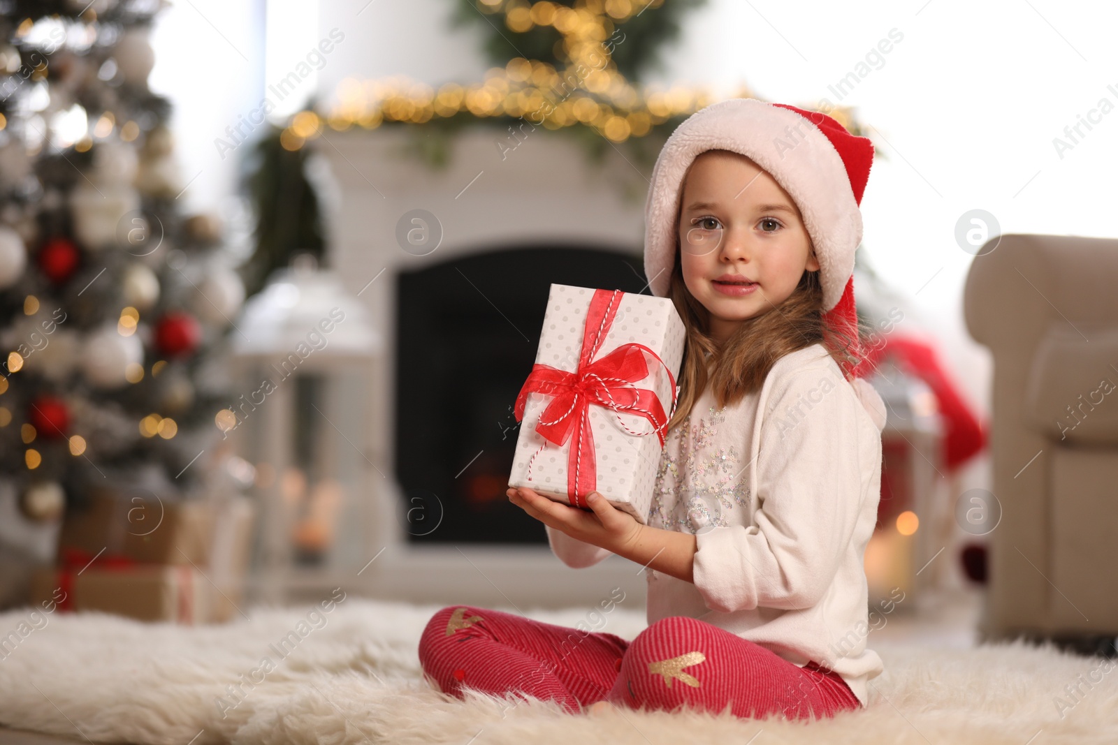 Photo of Cute little girl holding gift box in room decorated for Christmas