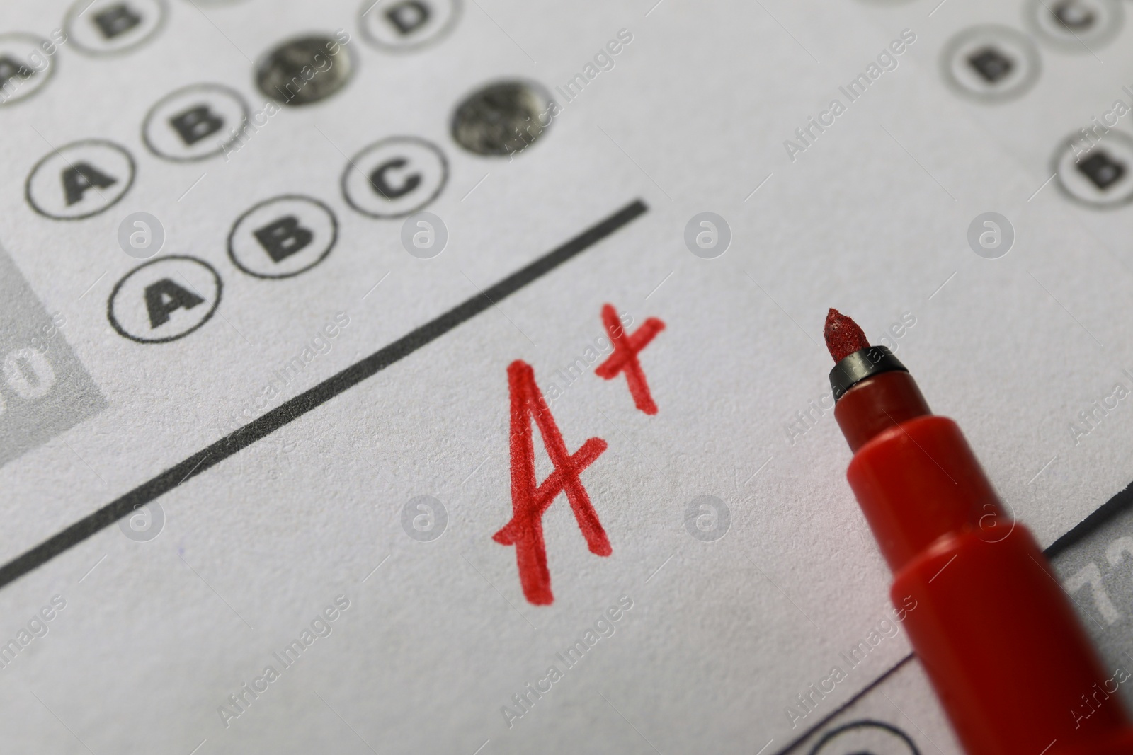 Photo of School grade. Letter A with plus symbol on answer sheet and red marker, closeup