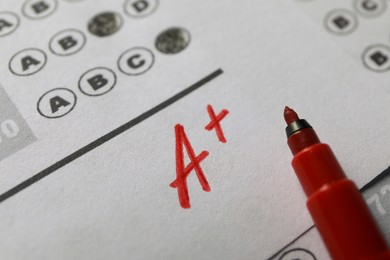 School grade. Letter A with plus symbol on answer sheet and red marker, closeup