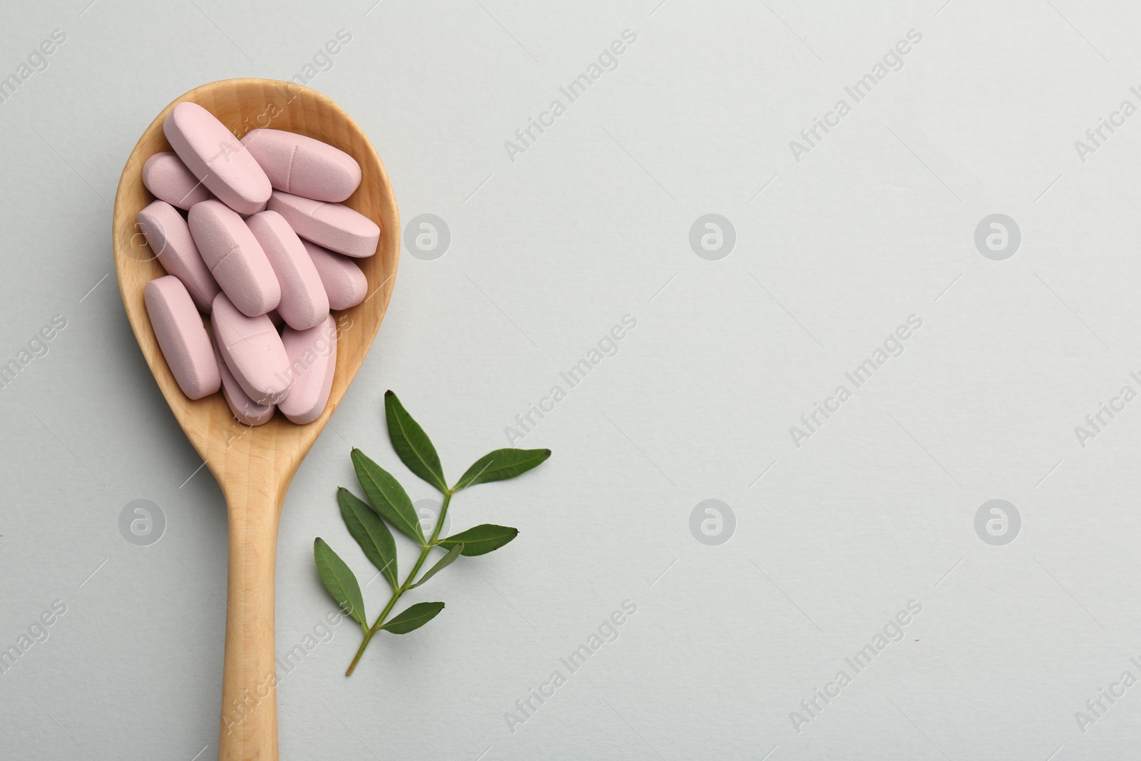 Photo of Vitamin pills in wooden spoon and twig on light grey background, top view with space for text. Health supplement