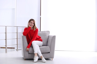 Photo of Attractive young woman sitting in armchair indoors. Space for text