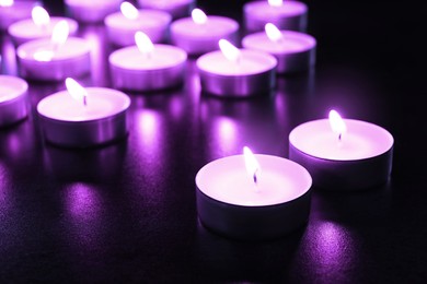 Image of Beautiful burning violet candles on black background, closeup. Funeral attributes