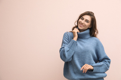 Photo of Beautiful young woman wearing warm blue sweater on light pink background. Space for text