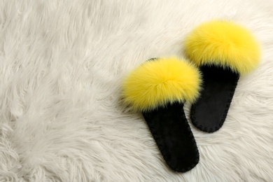 Photo of Pair of soft slippers on white faux fur, flat lay. Space for text