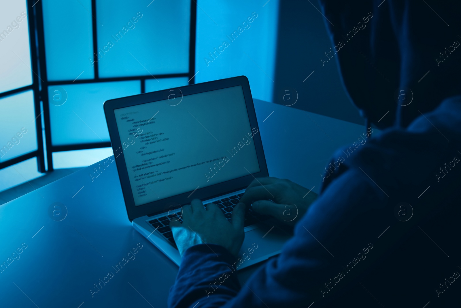 Photo of Man using laptop at table in dark room, closeup. Criminal offence