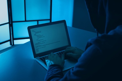 Photo of Man using laptop at table in dark room, closeup. Criminal offence