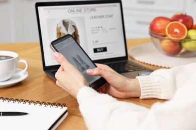 Photo of Woman with laptop and smartphone shopping online at wooden table in kitchen, closeup
