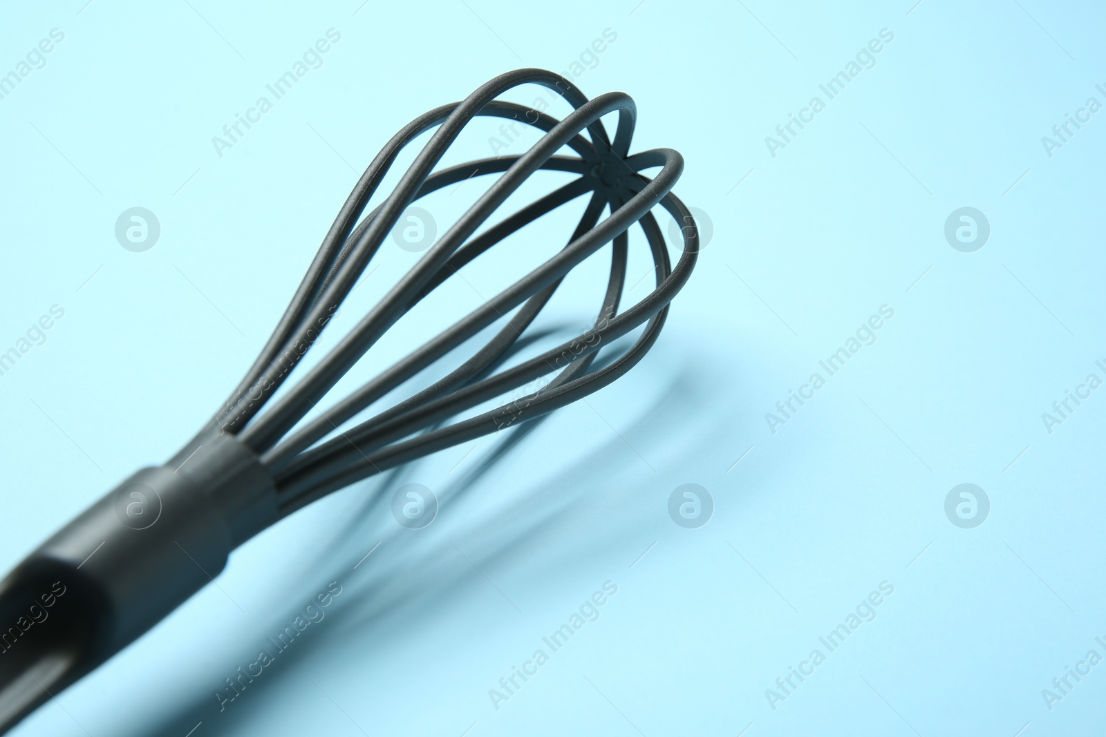 Photo of One whisk on light blue background, closeup. Space for text