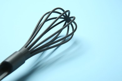 One whisk on light blue background, closeup. Space for text