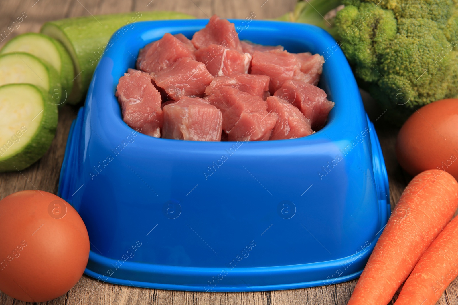 Photo of Raw meat in bowl and healthy products for pet on wooden background, closeup