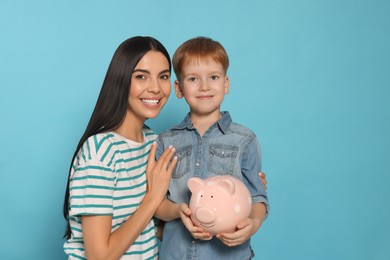 Mother and her son with ceramic piggy bank on light blue background