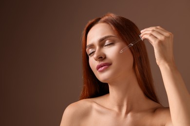 Photo of Beautiful young woman applying cosmetic serum onto her face on brown background, space for text