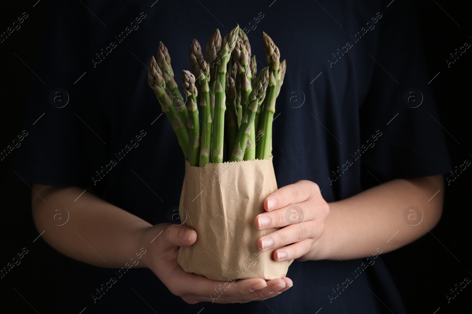 Photo of Woman with fresh asparagus on black background, closeup