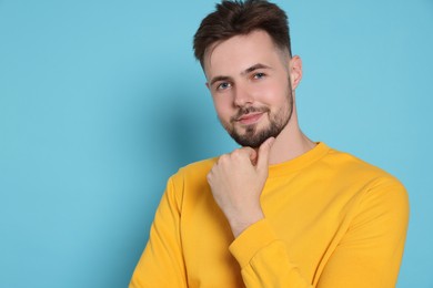 Handsome man in yellow sweatshirt on light blue background, space for text