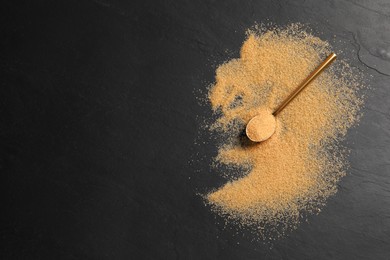 Photo of Brown sugar and spoon on black table, flat lay. Space for text