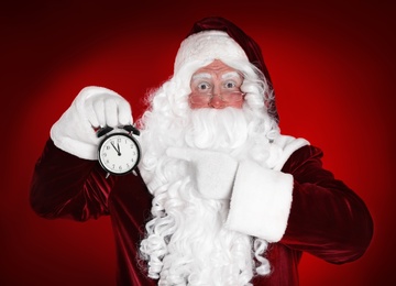 Santa Claus holding alarm clock on red background. Christmas countdown