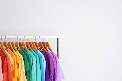 Photo of Rack with rainbow clothes on light background