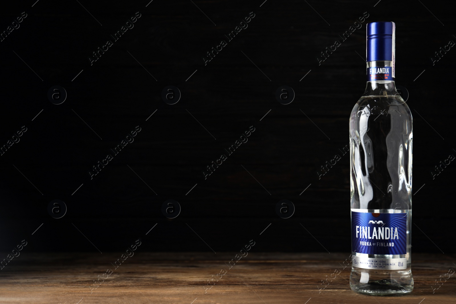 Photo of MYKOLAIV, UKRAINE - OCTOBER 03, 2019: Bottle of Finlandia vodka on wooden table against black background. Space for text