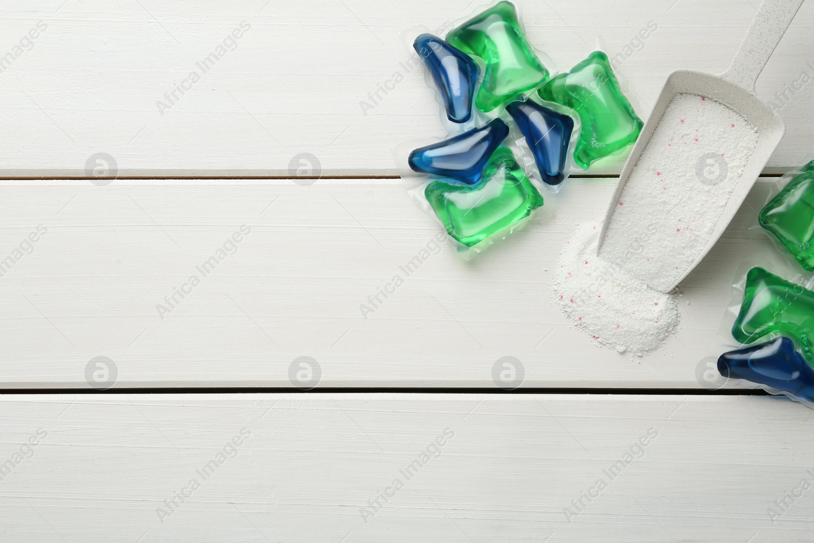 Photo of Laundry capsules and detergent powder on white wooden table, flat lay. Space for text